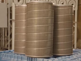 Replacement dust collector cartridge filters stacked in front of a dust collection system in an industrial facility.