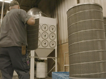 A technician walking towards an indusrial dust collector carrying a replacement cartridge filter.
